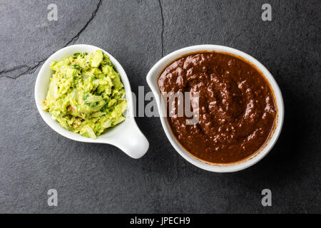 Traditional famous mexican sauces chocolate chili mole poblano, and avocado guacamole on slate gray background. Stock Photo