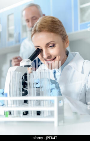 caucasian smiling chemist in white coat working with microscope and reagents while in chemical lab Stock Photo