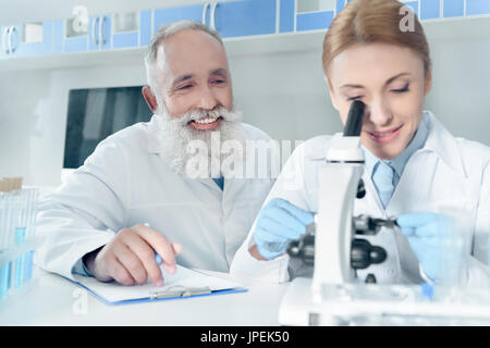 two happy scientists in white coats working together with microscope in chemical laboratory Stock Photo