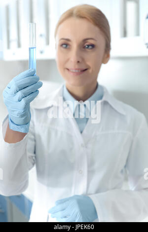 caucasian smiling chemist in uniform working in lab and looking at tube with reagent in chemical lab Stock Photo