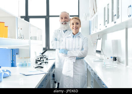 two happy chemists in white coats standing in chemical laboratory with microscopes and flasks Stock Photo