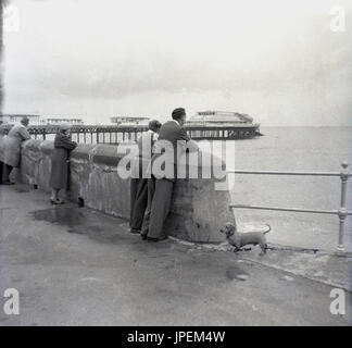 Late 1940s, young boy with father standing together looking over the sea and the victorian iron pier with pavilion theatre, at Cromer, Norfolk, England. Appearing at the theatre at this time were the famous Dazzle summer shows. Stock Photo