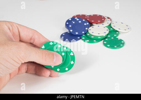 Gambler placing a bet on his cards holding two green casino chips over a white background with copy space Stock Photo