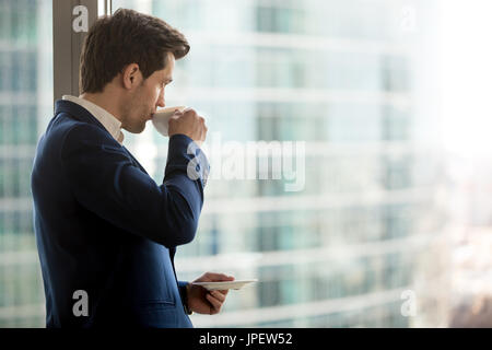 Thoughtful businessman drinking coffee, looking through office w Stock Photo
