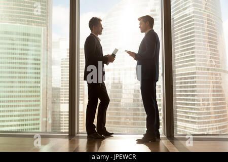 Two businessmen talking negotiating standing near big window, ci Stock Photo