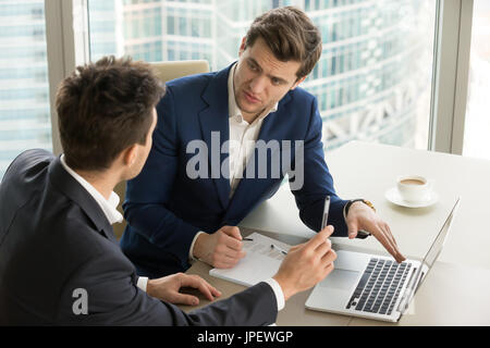 Two serious businessmen using laptop, discussing new project at  Stock Photo
