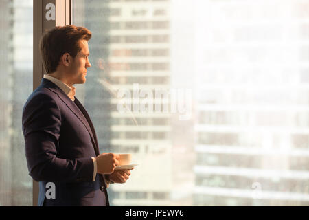 Serious pensive businessman drinking coffee, looking at sunrise  Stock Photo