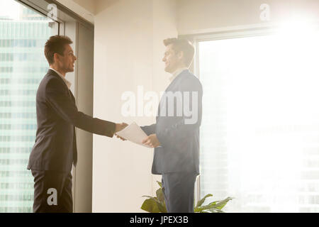 Two smiling businessmen shaking hands while standing in sunny of Stock Photo