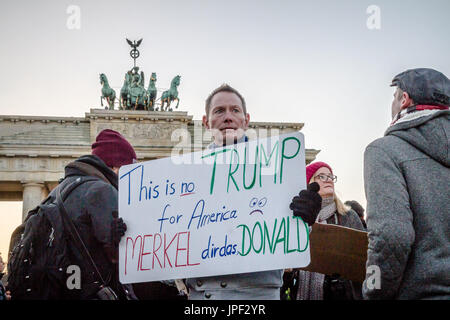 A man is holding an anti-Trump placard in front of the Brandenburg Gate in Berlin to protest the election of Donald Trump to president. Stock Photo