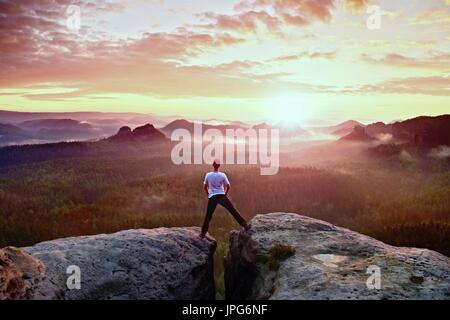 Crazy jumping hiker in black celebrate triumph between two rocky peaks. Wonderful daybreak. Stock Photo
