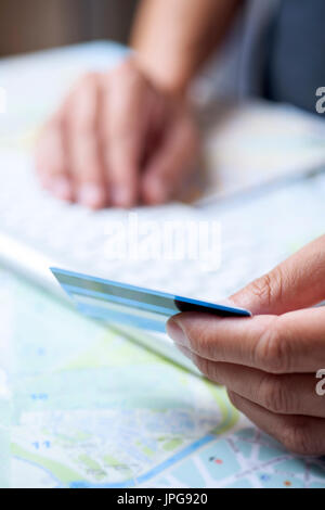 closeup of a young caucasian man using a credit card to book a trip online, using his computer, on a table full of maps Stock Photo