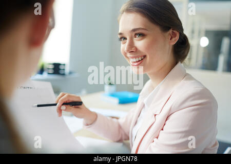 Smiling accountant pointing at financial document in her hand while talking to colleague Stock Photo