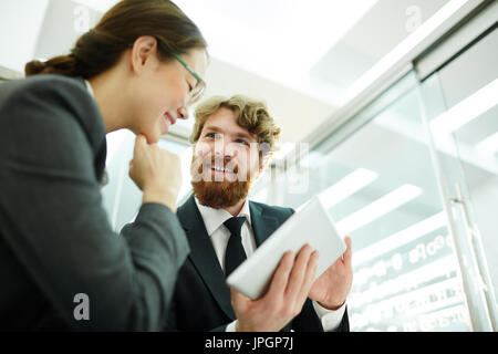 Portrait of enthusiastic bearded businessman showing data at digital tablet  to colleague discussing project in office Stock Photo