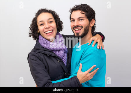 Happy couple with winter clothes. Hugging each other, they are smiling and looking at camera. Stock Photo