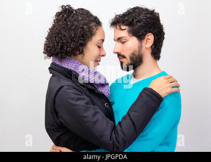 Woman with short curly hair is holding bearded man. They have eyes closed and winter / fall clothes. Isolated on white background. Stock Photo
