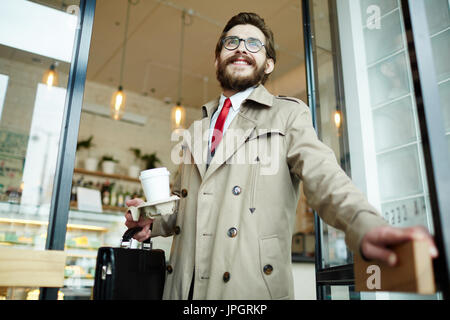 Young businessman with briefcase and drink leaving cafe Stock Photo