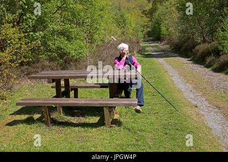 Senior woman walker sitting on picnic bench on forest walk Elsan Valley UK Stock Photo