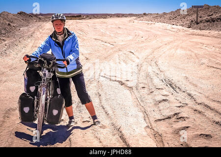 Woman cyclist struggling and pushing her bike on the sandy corrugated road in Altiplano in Bolivia Stock Photo