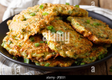 Hot zucchini pancakes with green onions on a plate close-up on a table. Horizontal Stock Photo
