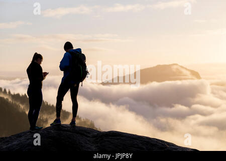 Hikers couple in the mountains above the clouds against sunset Stock Photo