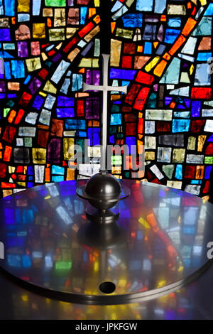 Abstract colors in a stained glass window mosaic reflected in a baptismal font cover with cross in a Toronto Roman Catholic church Stock Photo