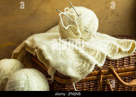 Handmade knitwear, clew of white wool yarn on vintage hobby and crafts wicker chest, wool clews, wood table, cozy atmosphere, shabby chic style Stock Photo