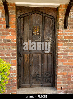 Dark brown wooden door of historic cottage with decorative hinges, in red brick wall in English village Stock Photo