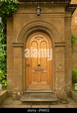 Elegant carved arched golden brown wooden door in ornate stone entrance to English cottage at Adderbury, England Stock Photo