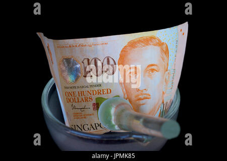 Singaporean hundred dollar note in a glass mortar and a pestle. Stock Photo