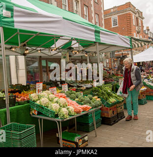 Fruit & vegetable stall with elderly woman looking at colourful fresh produce under green & white awning at street market in Winchester, England Stock Photo