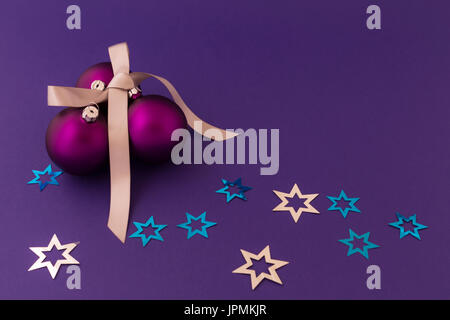 Beautiful purple christmas balls with satin effect, grey gift ribbon and metallic silver and blue stars on purple background. Stock Photo