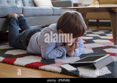 Boy with hand on chin looking at tablet computer while lying on carpet Stock Photo