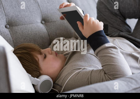 Close up of boy wearing headphones while using digital tablet on sofa at home Stock Photo