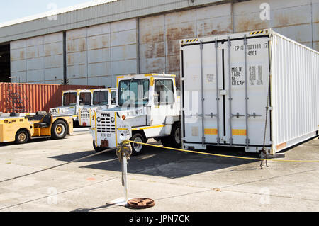 A yard truck beside a shipping container on a concrete tarmac in front of a warehouse. Stock Photo