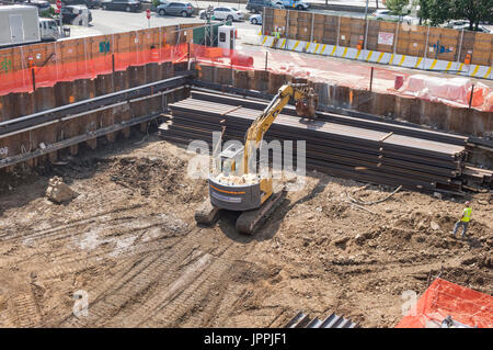 A tracked bucket excavator used as a rotating grab mover with continuous tracks and lifting crane on a construction site in New York City Stock Photo