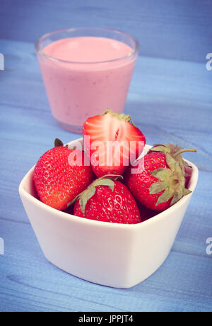 Vintage photo, Fresh ripe strawberries in bowl and cup of delicious milkshake on boards, concept of healthy dessert and nutrition