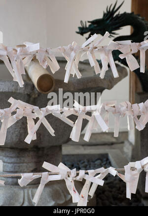 Close up of O-mikuji tied on rope near a fountain at Seiganji Temple in Kyoto Stock Photo