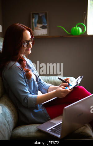 Freelance modern concept. Side view of woman on couch correcting documents. Stock Photo