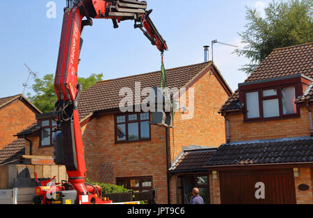 And out she comes, a large Henry Milnes Lathe is lifted from the rear of a property out througha gap between houses to the waiting lorry for transport Stock Photo