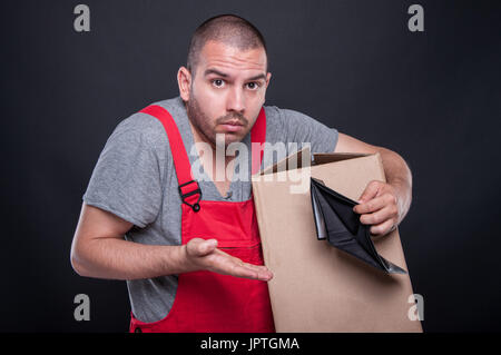 Confused mover man holding box showing empty wallet on black background Stock Photo