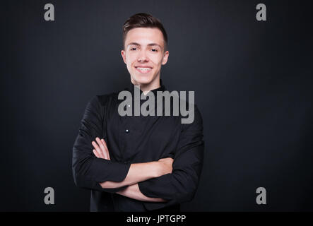 Portrait of attractive male chef with crossed arms smiling on black studio background Stock Photo