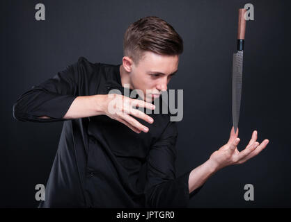 Talented cook or chef making magic with his knife on dark studio background Stock Photo