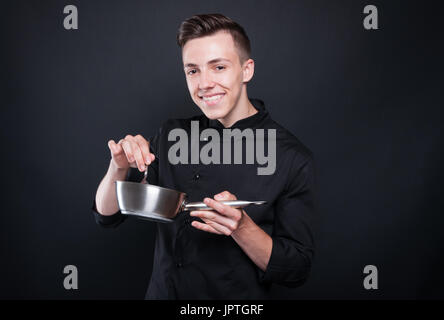 Joyful young cook stirring with spoon in saucepan preparing tasty meal Stock Photo
