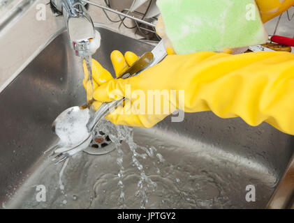 Woman hands rinsing cutlery under running water in the sink in close up view Stock Photo