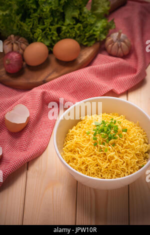 Instant noodles in bowl with vegetables on wood background Stock Photo