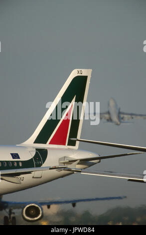 tail-fin of an Alitalia Airbus A321-100, wing and CFM56-3 jet-engine of a Boeing 737-300 taxiing and a Boeing 747 climbing out after take-off behind Stock Photo