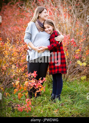 Happy young pregnant mother hugging with teen daughter in autumn park. Happy family concept Stock Photo