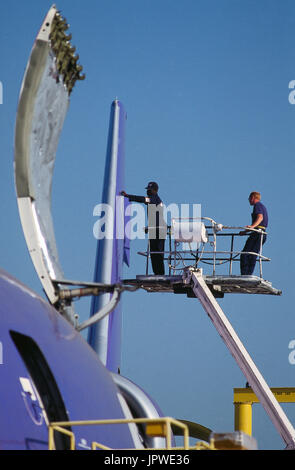 maintenance engineers in a cherry picker working on the tail-fin of a DC-10, black man working whilst the white man watches Stock Photo