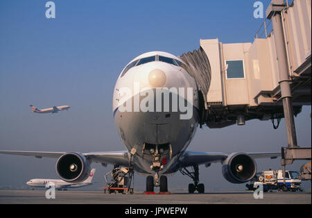 nose of an ANA Boeing 767 parked with a jetway attached, Japan Air System JAS Airbus A300 climbing out after take-off and Japan Airlines 777 taxiing b Stock Photo