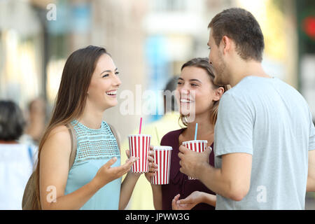 Three happy friends talking and holding refreshments in the street Stock Photo